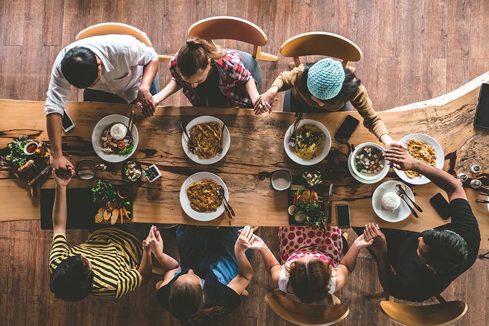 friends hold hands and pray around dinner table