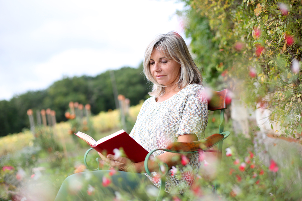 woman reading a book outside in a garden