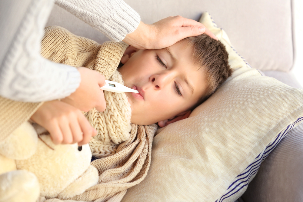 young boy sick at home while mom takes temperature