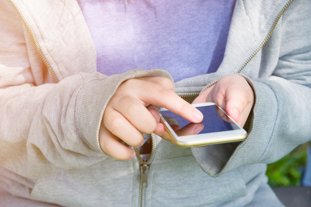 teen in hoodie uses smartphone
