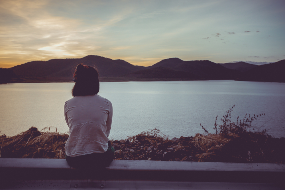 woman sits at the edge of a lake at sunset