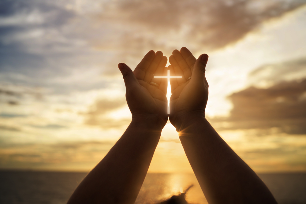 hands holding illuminated cross at sunset