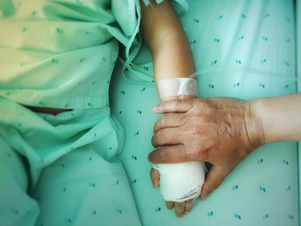 parent holds hand of sick child in hospital bed