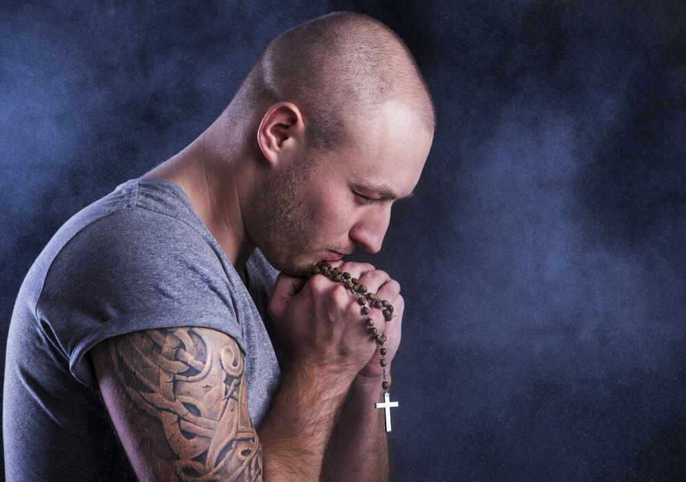 young man with tattoos prays rosary
