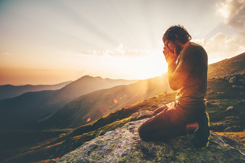 Man prays at sunset overlooking mountains