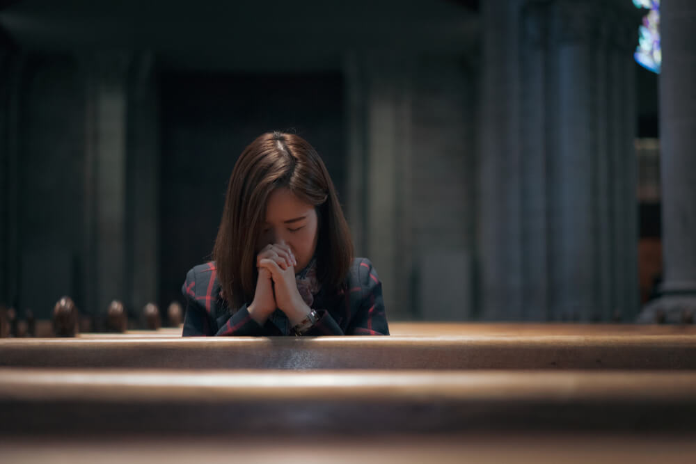woman prays in church pew