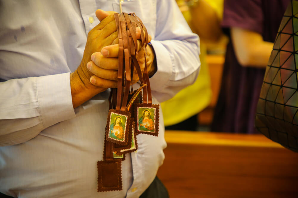 man holds handful of brown scapulars