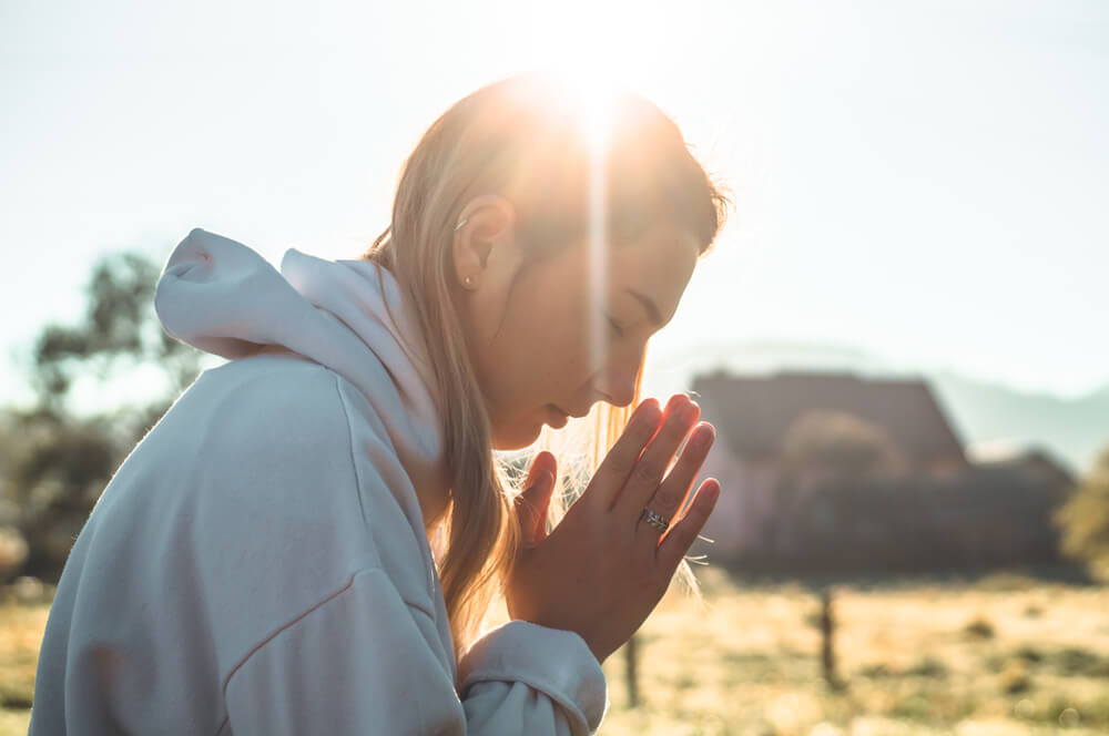 young woman prays at sunrise