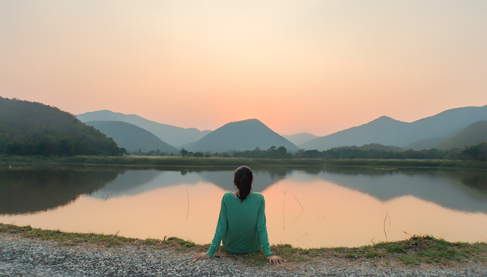 Woman sits beside a peaceful lake