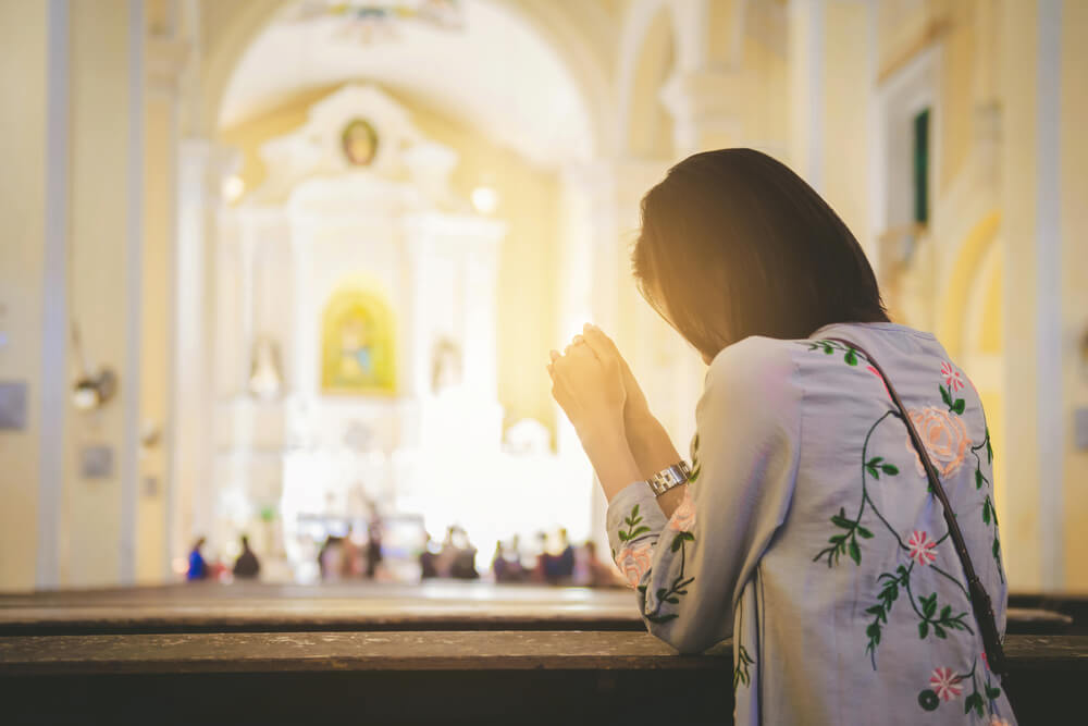 young woman kneels in prayer in church