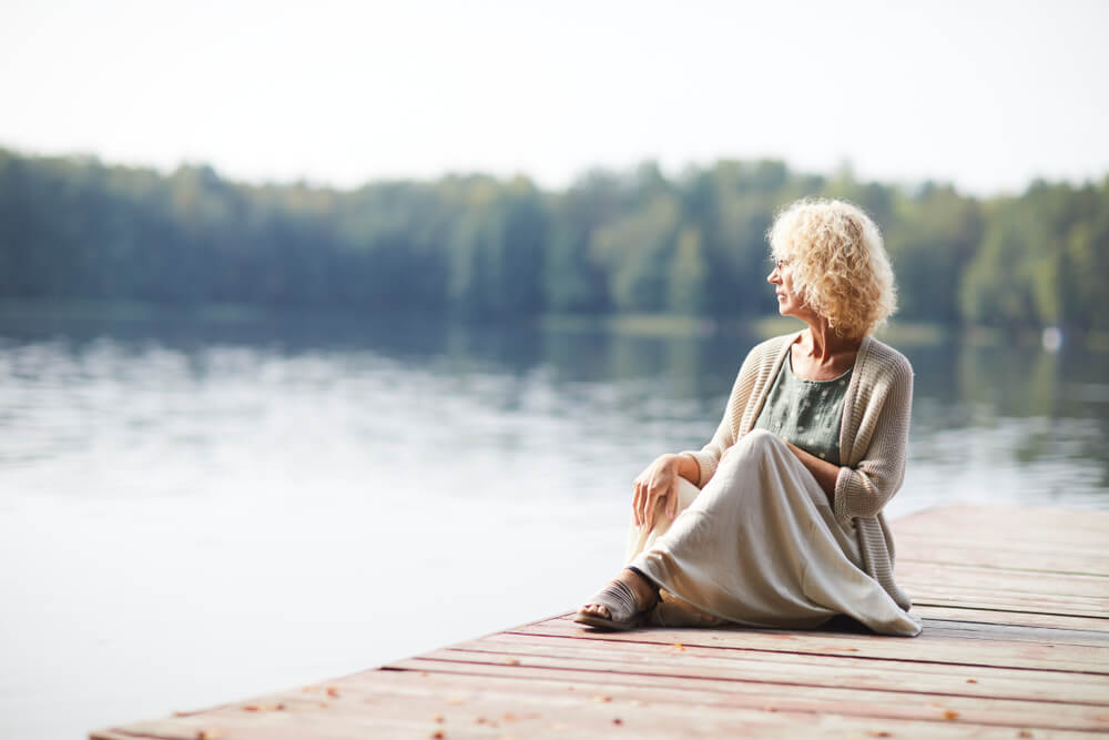 woman sits quietly on pier over lake