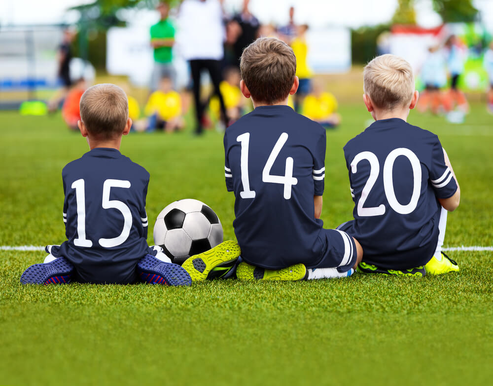 three boys sit on sidelines at soccer game