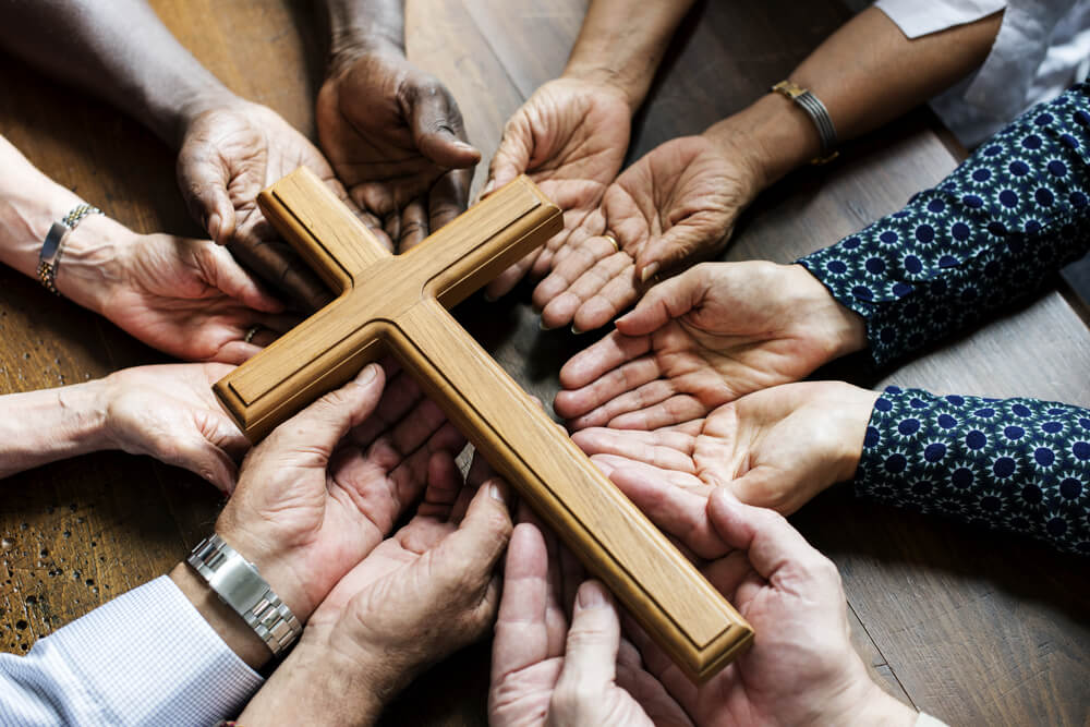 many hands reach in to touch cross