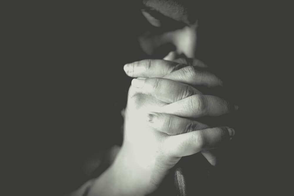 woman folds hands in prayer