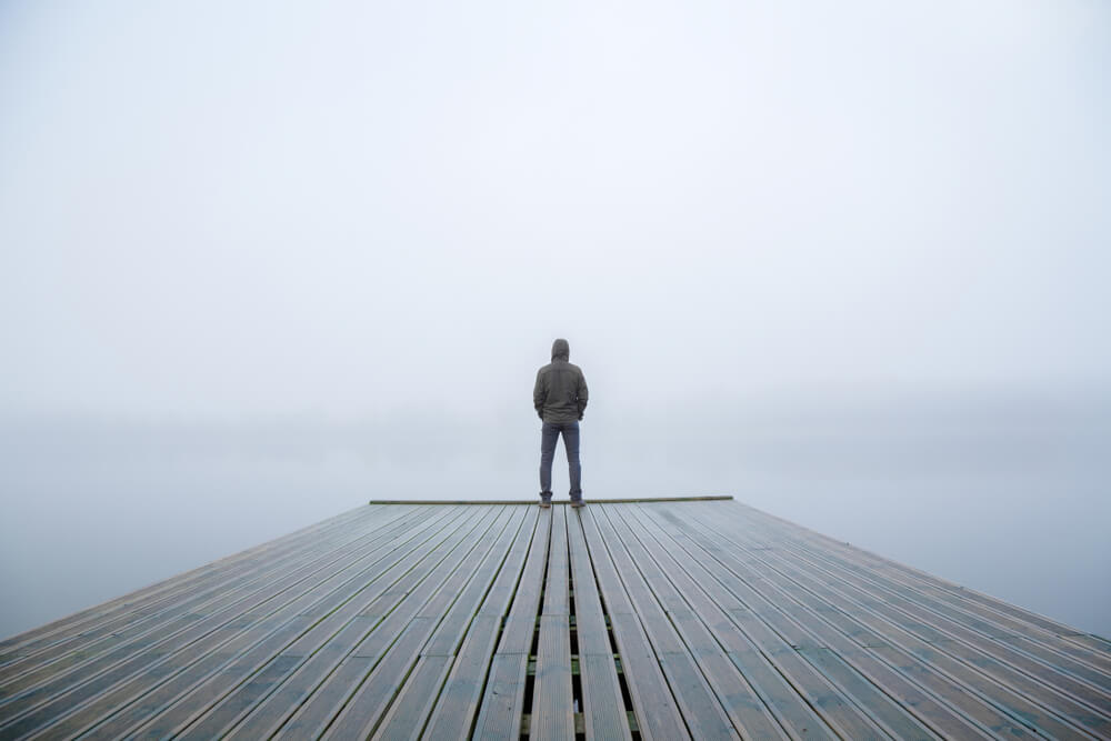 man stands in fog on pier