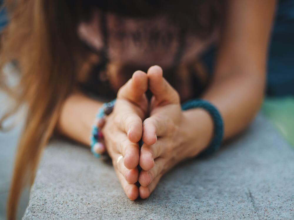 Woman folds hands in prayer