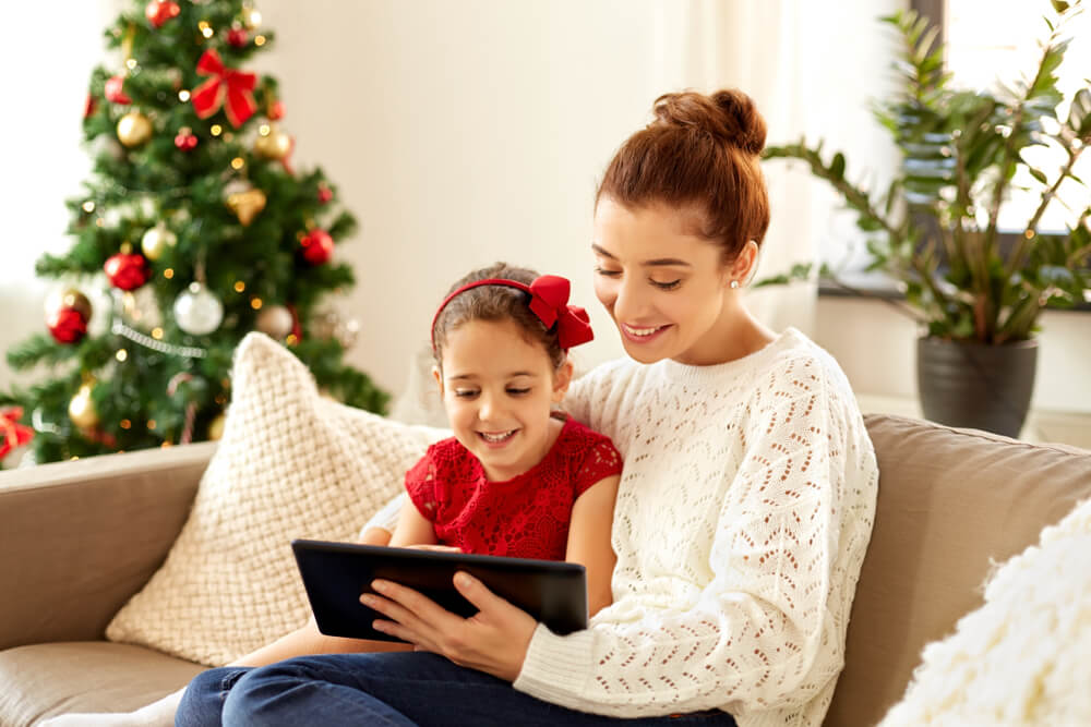 Mom and daughter look at tablet by the Christmas tree