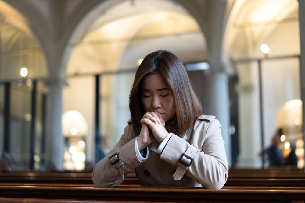 woman kneels in church in prayer