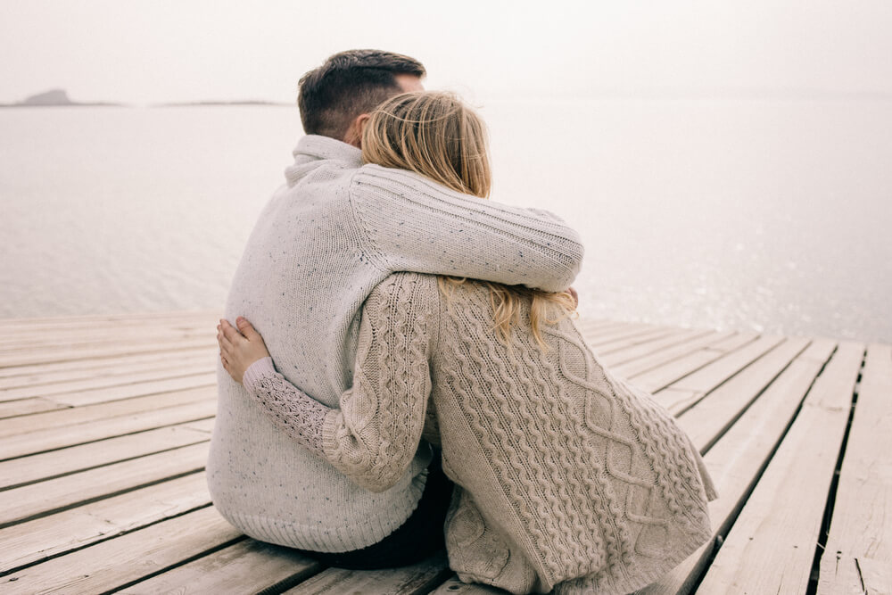 couple sits on pier, hugs