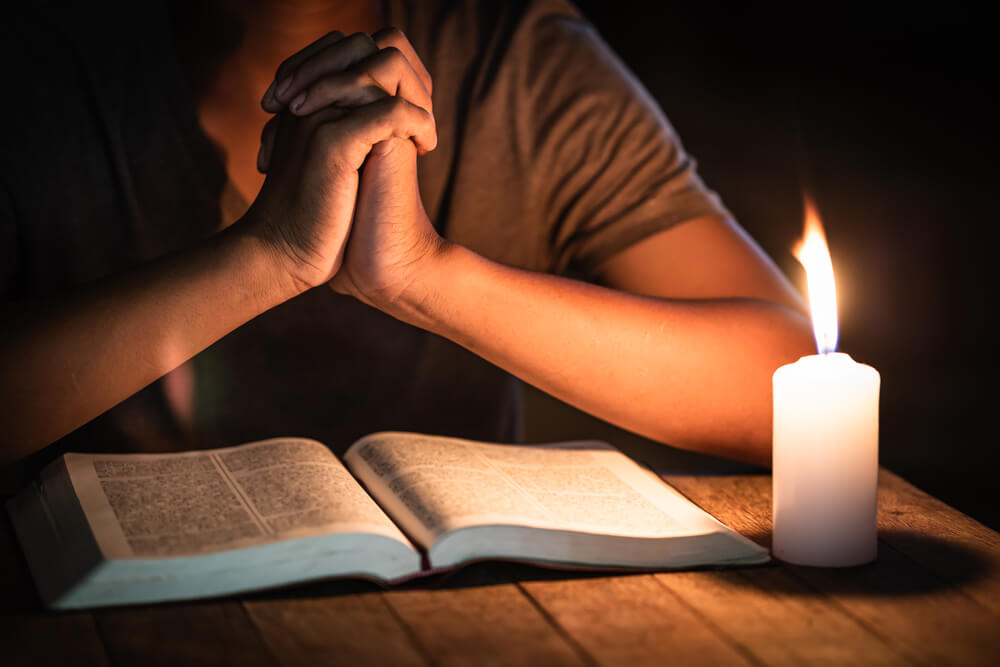 man prays and reads scripture by candlelight