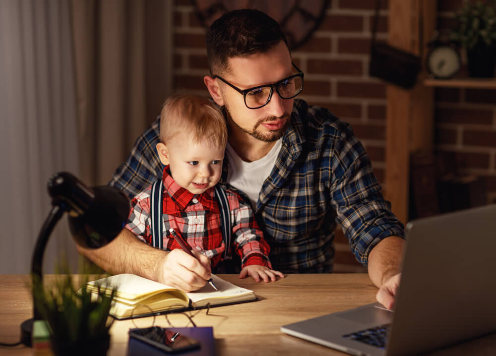 young dad works at home with his son in lap