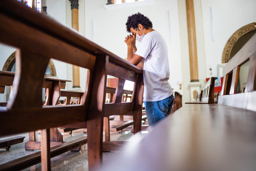 man kneels in a church in prayer