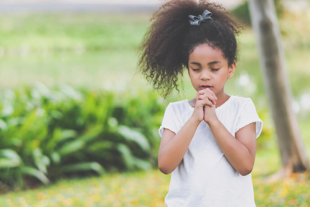 young girl focuses mind for prayer outdoors with eyes closed