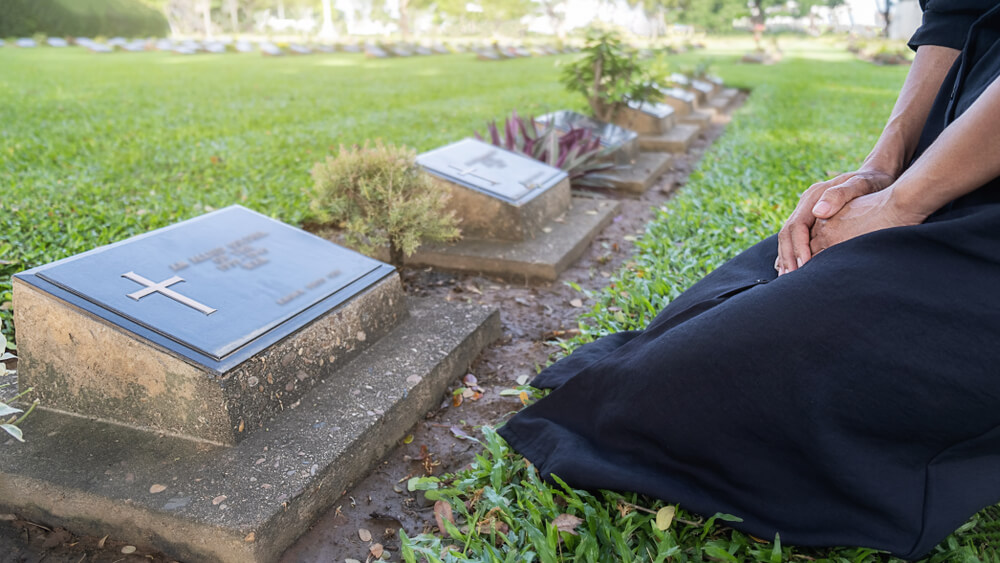 woman kneels beside the grave of a dead loved one
