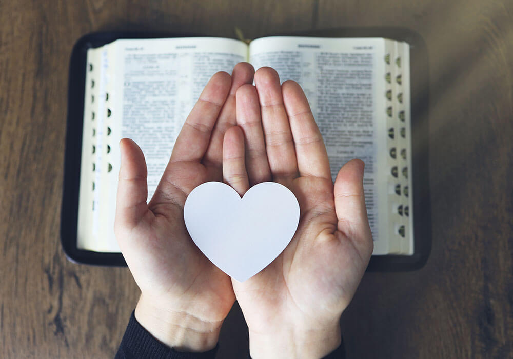 hands holing a white heart-shaped paper over the Bible